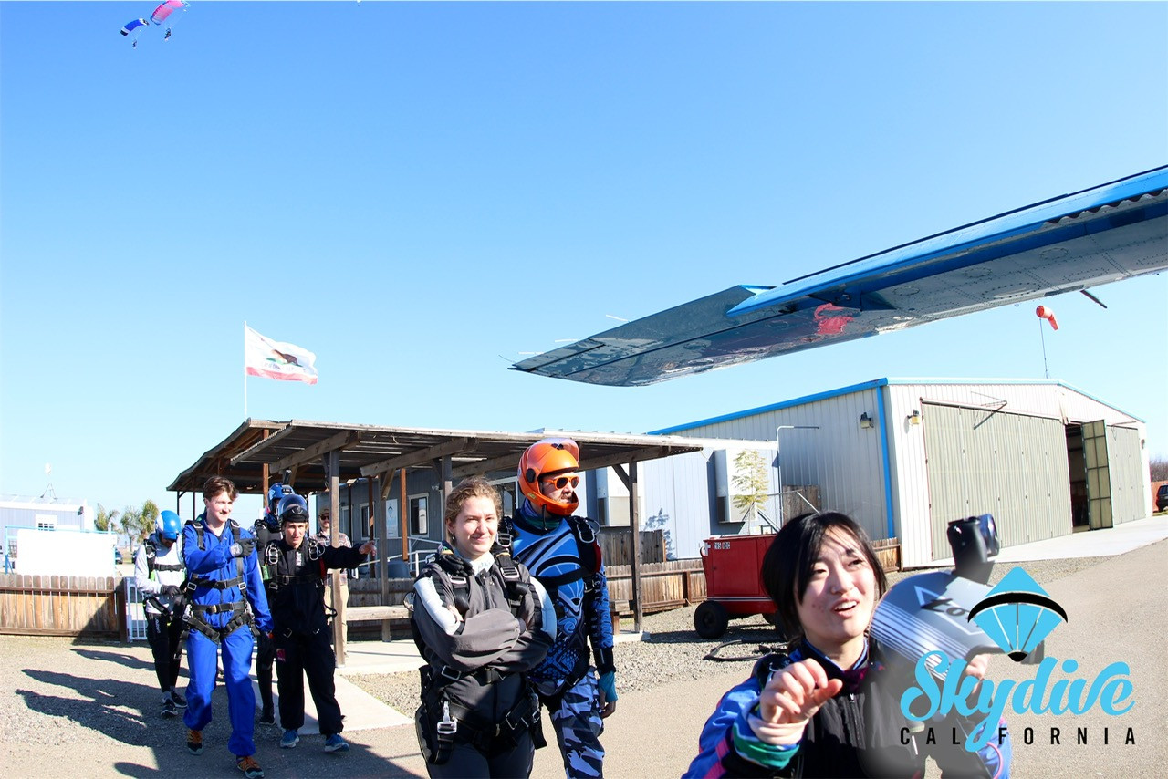 A tandem skydiver, suited up and ready, walks toward the aircraft with their instructor at Skydive California, anticipation building.