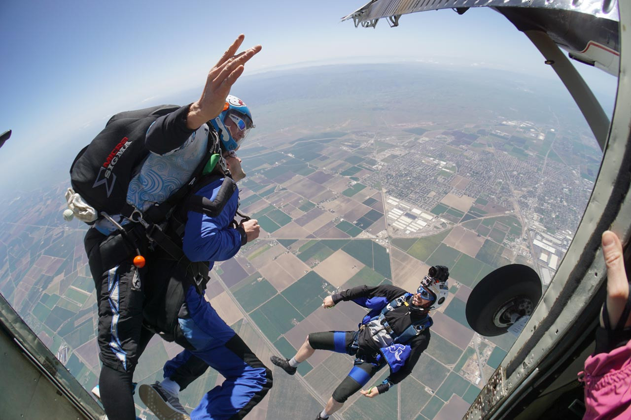 Tandem student and instructor leaping out of Skydive California airplane.